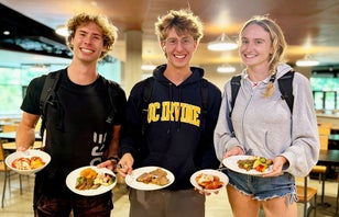 Three smiling students holding their plates of food in the dining hall.