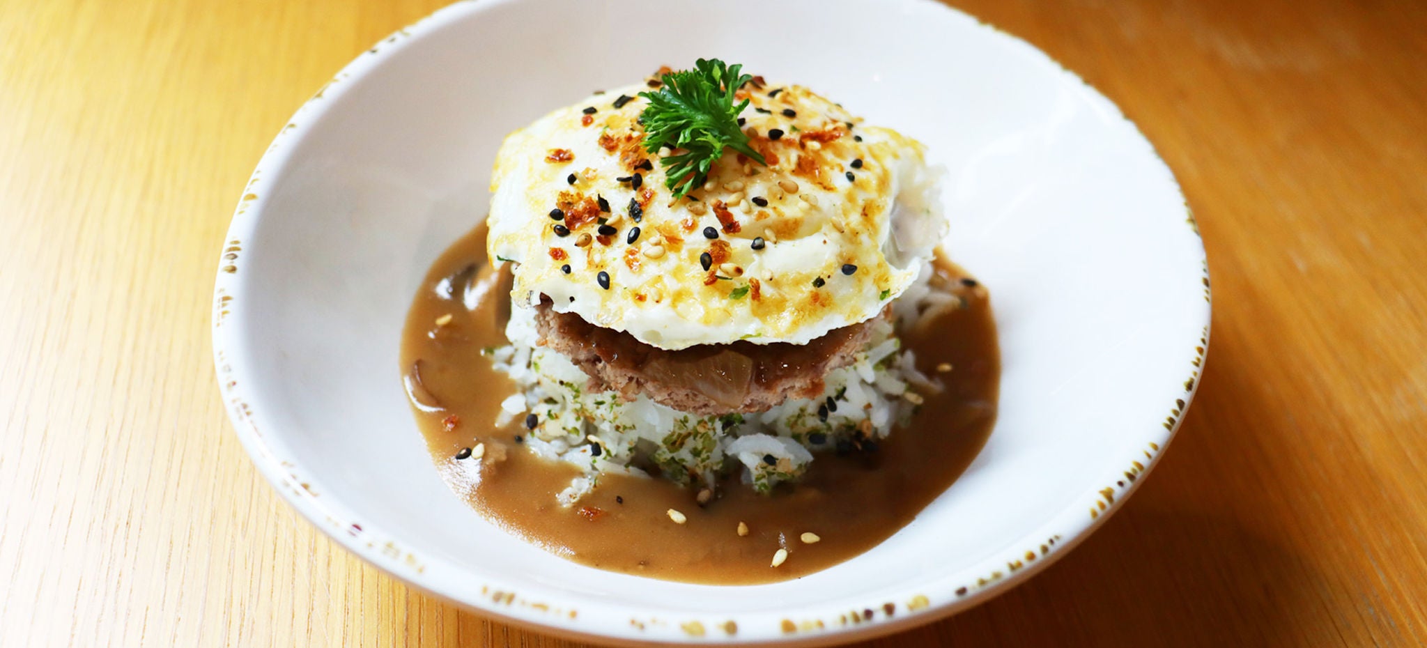 Loco moco in a bowl on a wooden table.