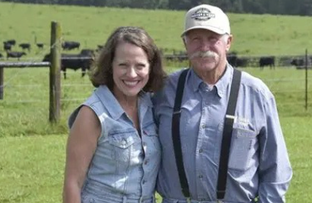 One male and one female farmer stand in a field in Alabama with their arms around each other