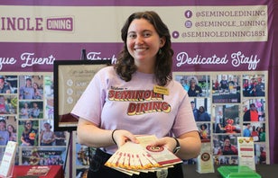 student employee poses in front of orientation banner with meal plan brochures