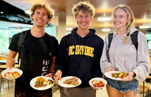 Three UCI students smiling, holding their plate of food.