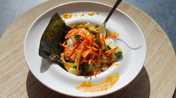 Sushi ingredients in a white bowl adorned with a piece of seaweed and a spoon