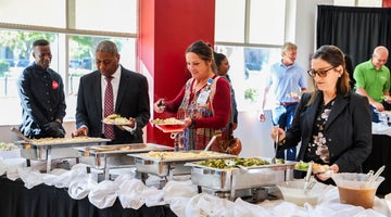 A group of people stand over a buffet of food serving themselves plates.