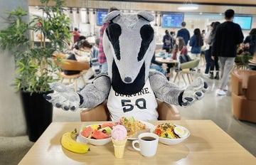 Peter the Anteater mascot is sitting at a table, with a lot of food in front of him.