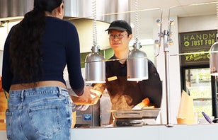 A dining hall employee handing a lady her plate of food.